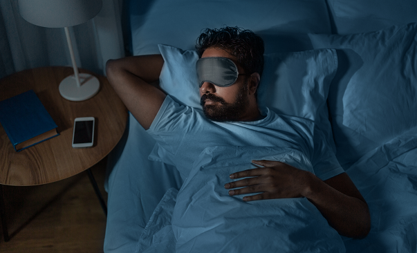 A person sleeping in bed with blindfold 
Description automatically generated