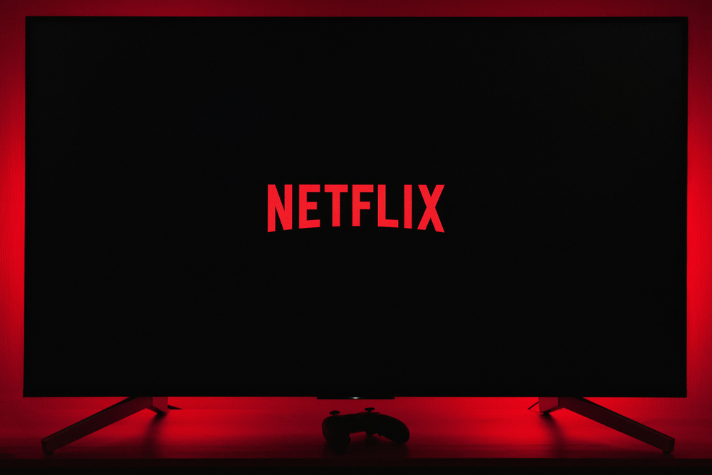 The Netflix logo showing on a black TV screen. A game controller is shown beneath the TV screen.