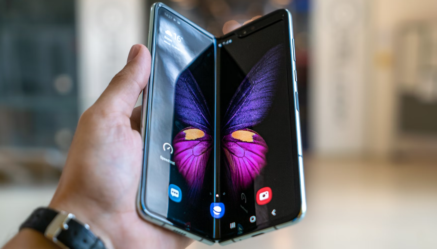 Close-up of a foldable smartphone partially open, displaying a vivid purple and yellow butterfly image across its dual screens.